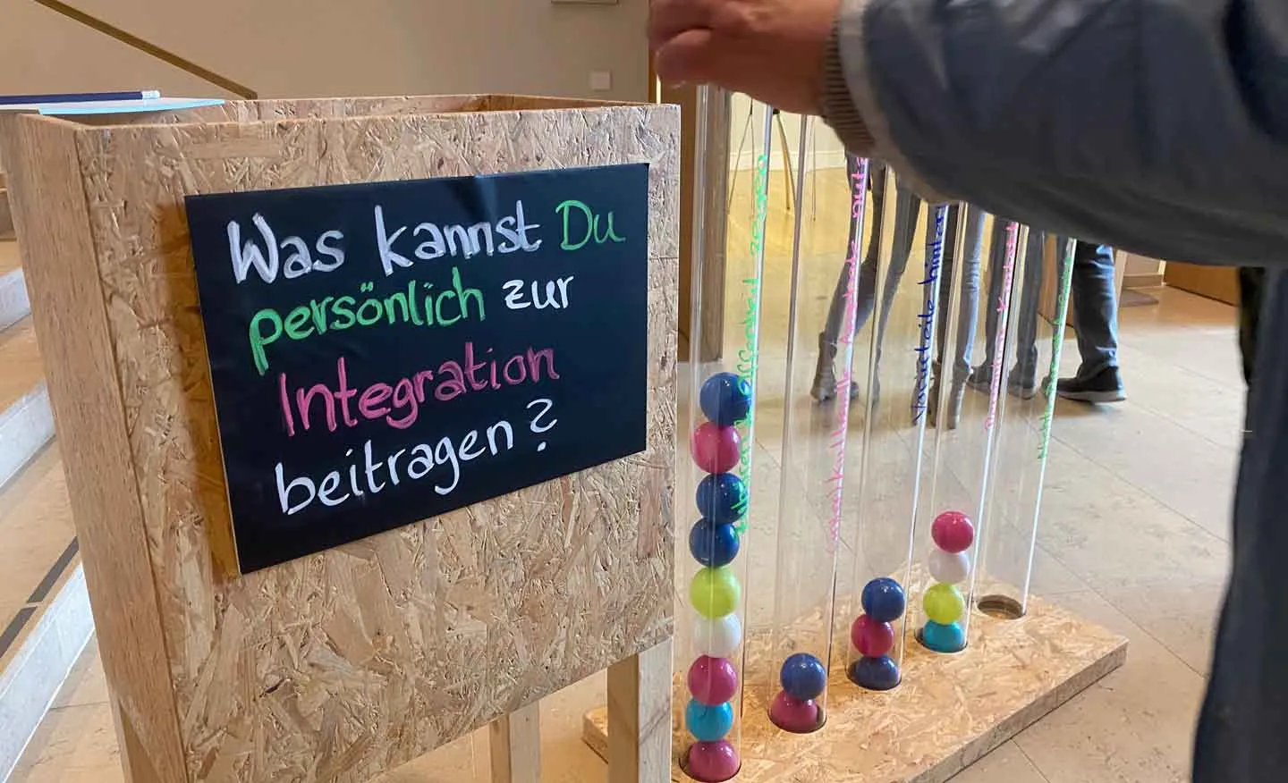 Ein Schild mit der Aufschrift "Was kannst Du persönlich zur Integration beitragen?" neben Röhren mit verschiedenen Antworten, in die Bälle geworfen wurden