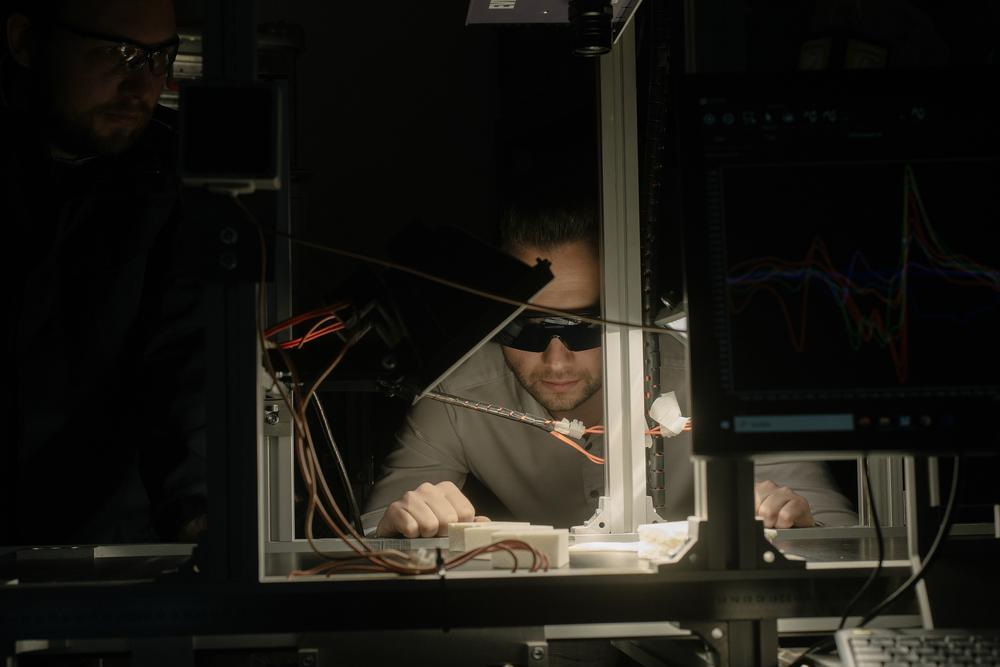 Ein Mann mit Laborbrille schaut in einem dunklen Raum auf einen Versuchsaufbau