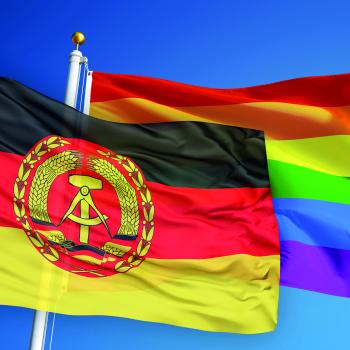 Eine DDR Flagge und eine Regenbogenflagge vor blauem Himmel