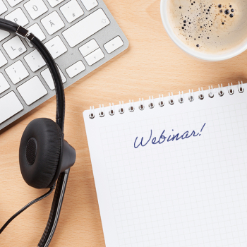 Tastatur, Kopfhörer, Kaffeetasse, Stift und Block mit Aufschrift "Webinar"